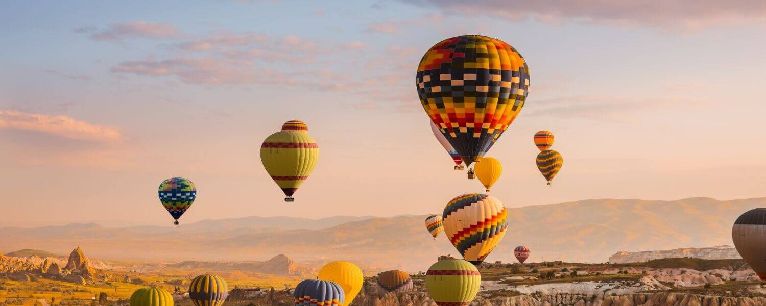 Colorful hot air balloons drifting over Cappadocia's Goreme Valley at sunrise, showcasing stunning rock formations.