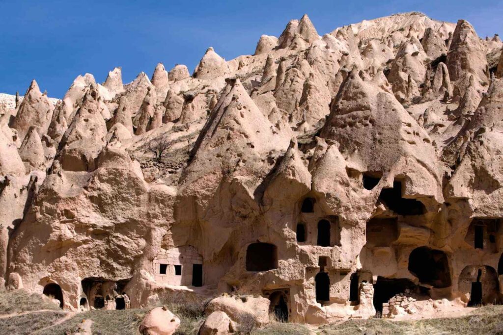 Ancient cave dwellings carved into Cappadocia's rugged, conical rock formations under a clear blue sky.