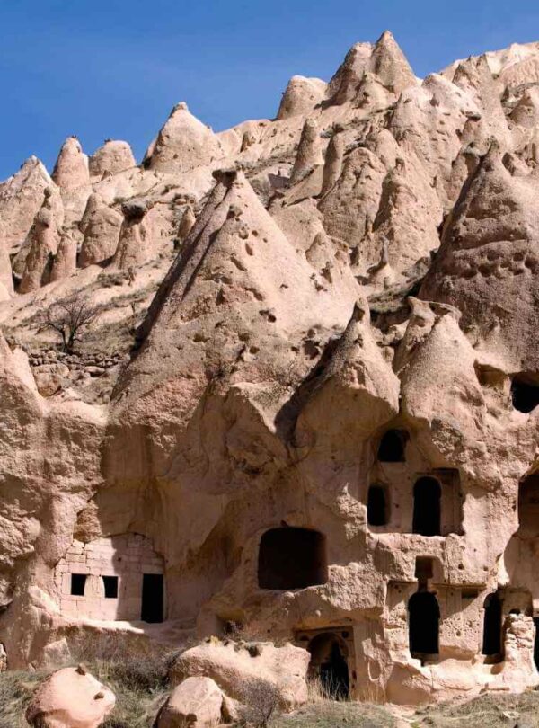 Ancient cave dwellings carved into Cappadocia's rugged, conical rock formations under a clear blue sky.