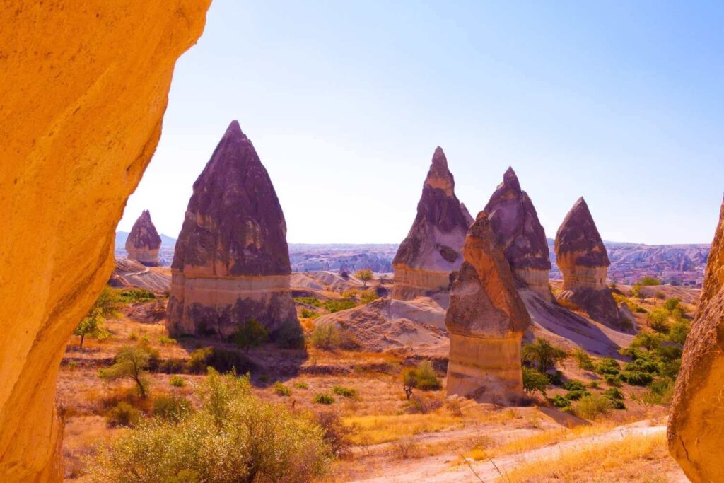 Unique conical rock formations known as fairy chimneys in Cappadocia, Turkey, under bright sunlight and a clear sky.