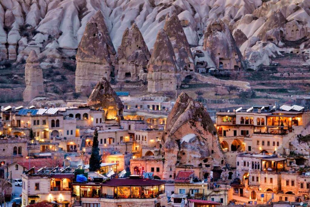 Illuminated cave town in Cappadocia, Turkey, with rock formations and traditional houses glowing at dusk.