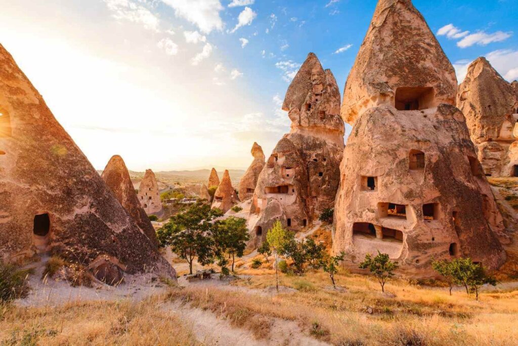 Unique rock formations with carved-out cave dwellings in Cappadocia, Turkey, under a bright sunset sky.