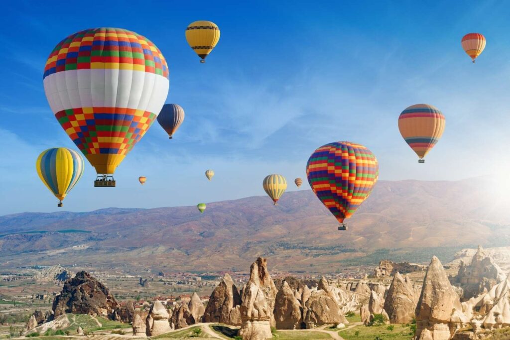 Vibrant hot air balloons soaring above Cappadocia's rugged terrain during sunrise, highlighting the region's unique rock formations.