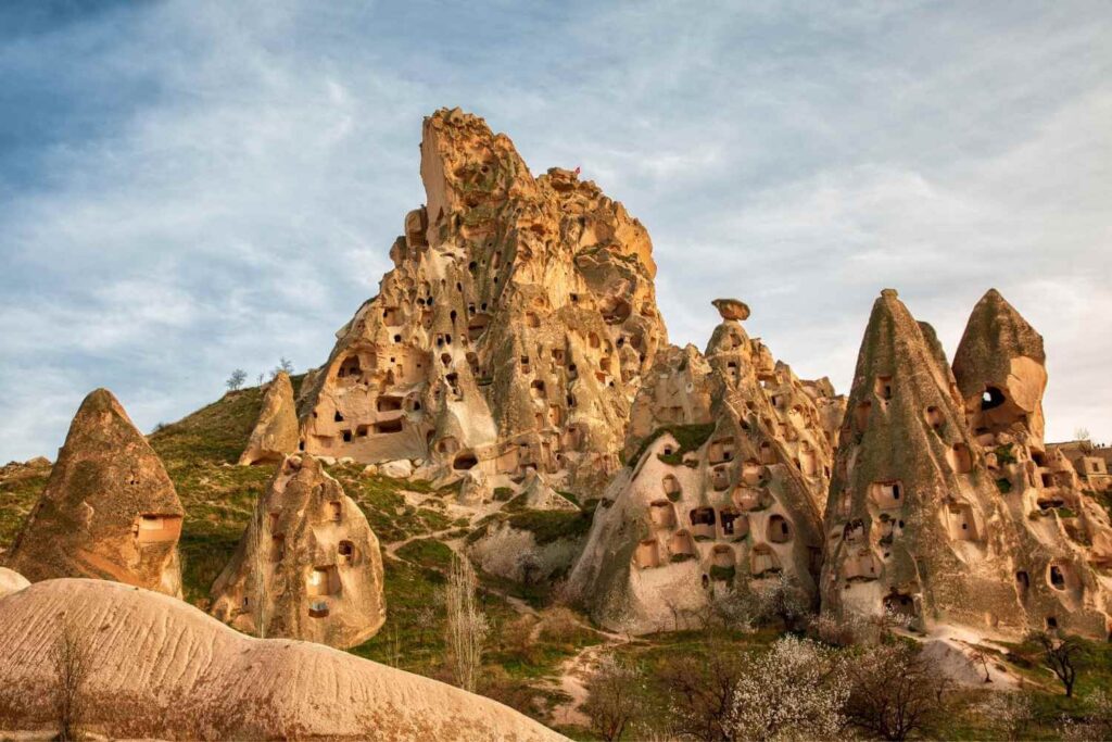 Rock formations in Cappadocia, Turkey, featuring numerous carved-out ancient cave dwellings on a grassy hillside.