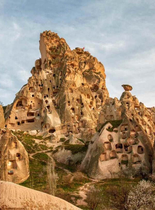 Rock formations in Cappadocia, Turkey, featuring numerous carved-out ancient cave dwellings on a grassy hillside.