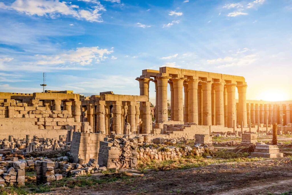 The Luxor Temple in Egypt, featuring towering stone columns and ancient ruins, bathed in warm golden sunlight during sunset.