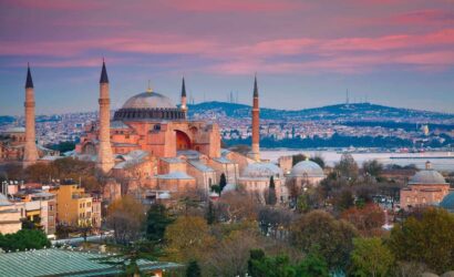 Hagia Sophia in Istanbul at sunset, featuring its domes and minarets with a cityscape and water in the background.