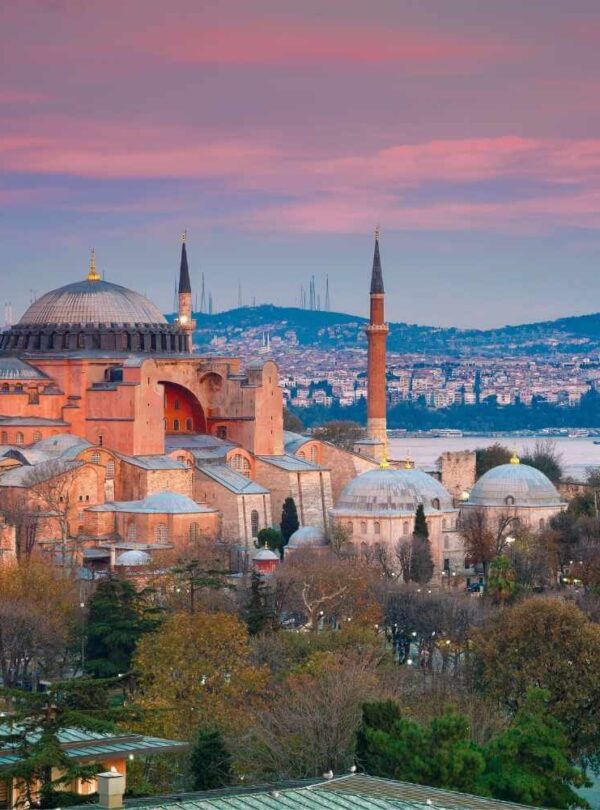 Hagia Sophia in Istanbul at sunset, featuring its domes and minarets with a cityscape and water in the background.