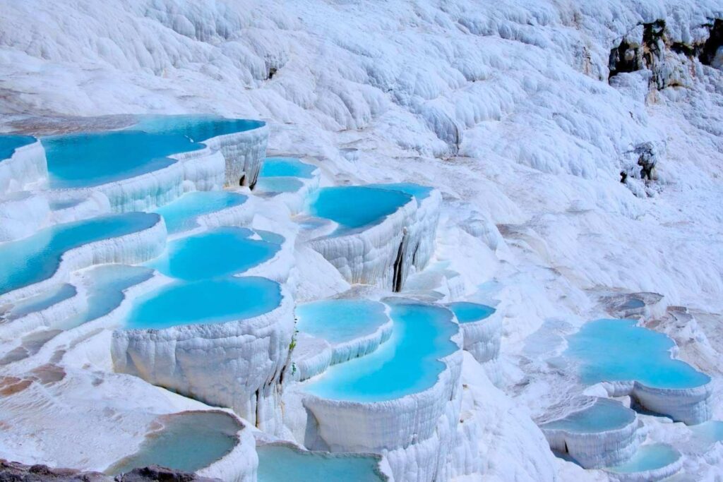 Stunning white travertine terraces filled with turquoise thermal waters in Pamukkale, Turkey, under a clear sky.