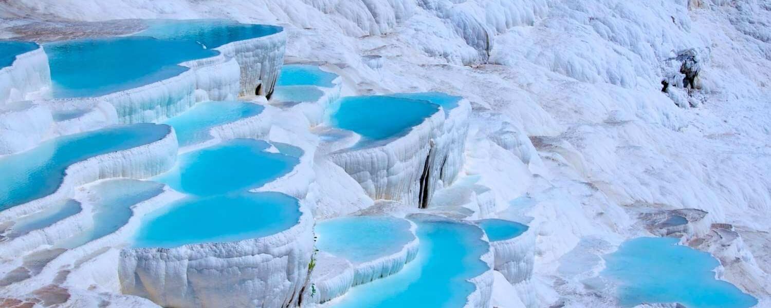 Stunning white travertine terraces filled with turquoise thermal waters in Pamukkale, Turkey, under a clear sky.