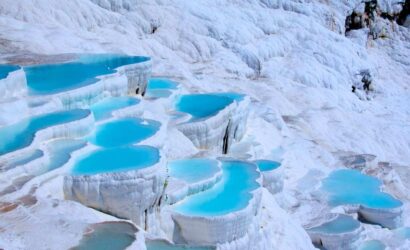 Stunning white travertine terraces filled with turquoise thermal waters in Pamukkale, Turkey, under a clear sky.