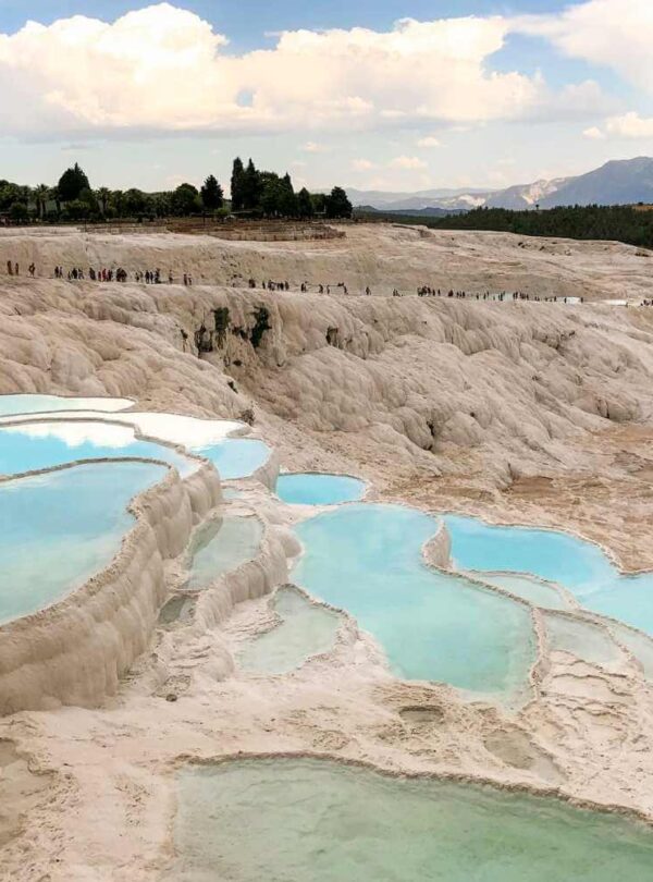 Stunning white travertine terraces of Pamukkale, Turkey, filled with turquoise thermal pools under a partly cloudy sky.