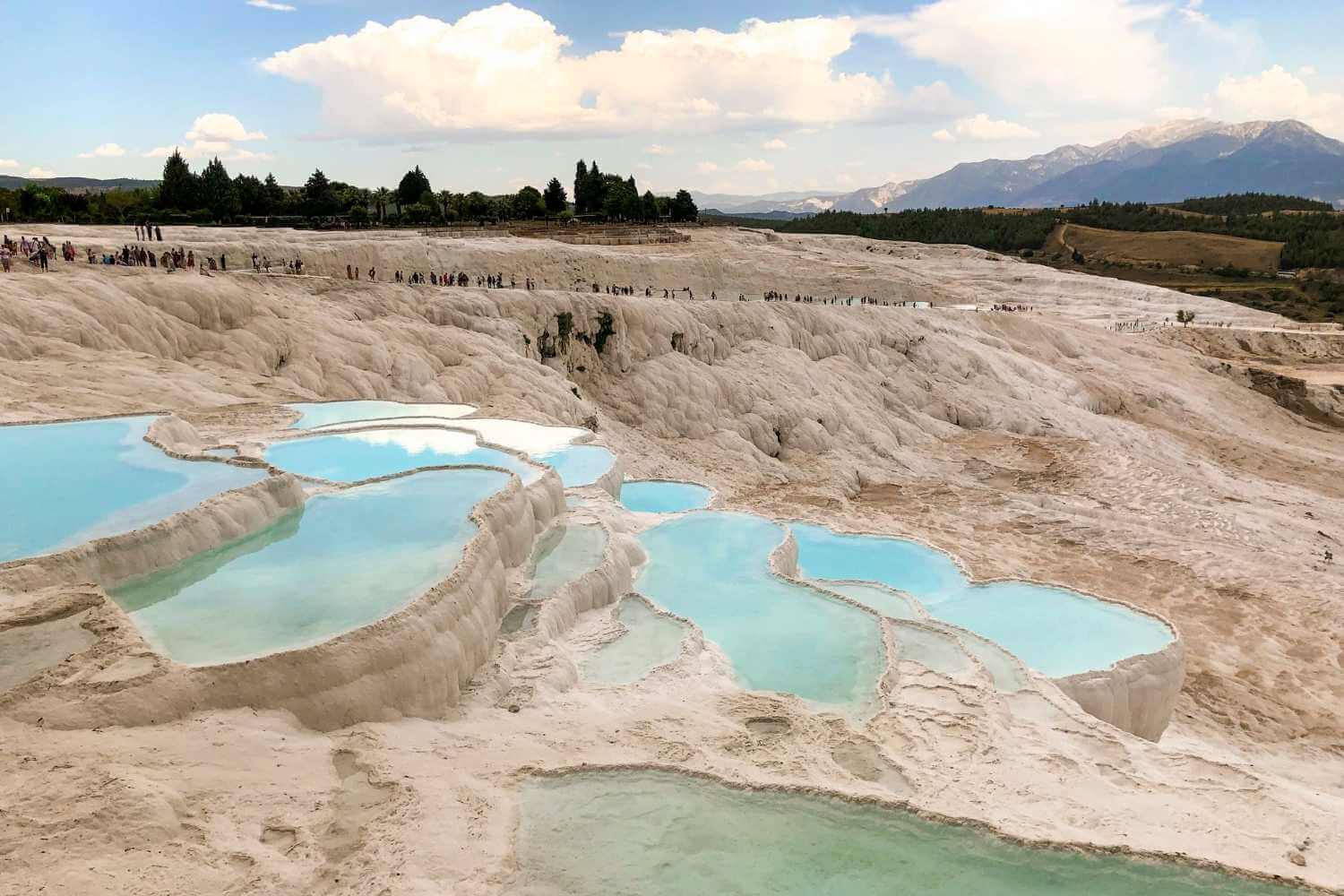 Stunning white travertine terraces of Pamukkale, Turkey, filled with turquoise thermal pools under a partly cloudy sky.