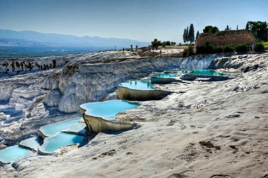 Crystal-clear turquoise pools on white travertine terraces at Pamukkale, Turkey, with tourists exploring the site.