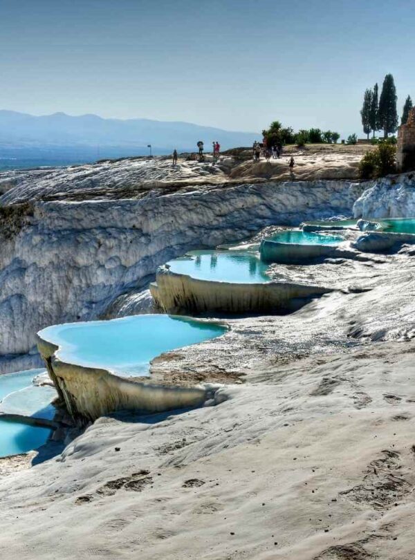 Crystal-clear turquoise pools on white travertine terraces at Pamukkale, Turkey, with tourists exploring the site.