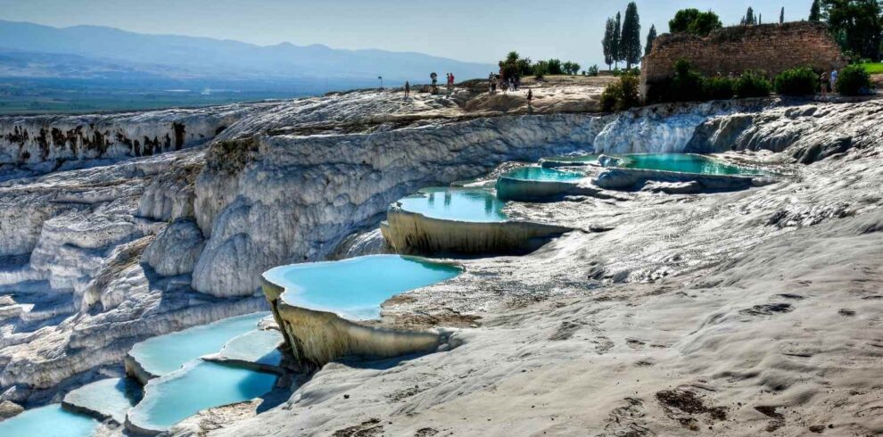 Crystal-clear turquoise pools on white travertine terraces at Pamukkale, Turkey, with tourists exploring the site.