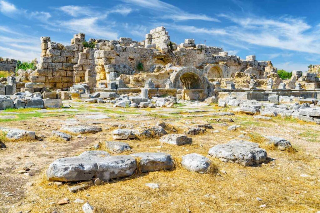 Remains of the Roman Baths in Side, Turkey, featuring stone walls, arches, and scattered ancient stones under a bright sky.