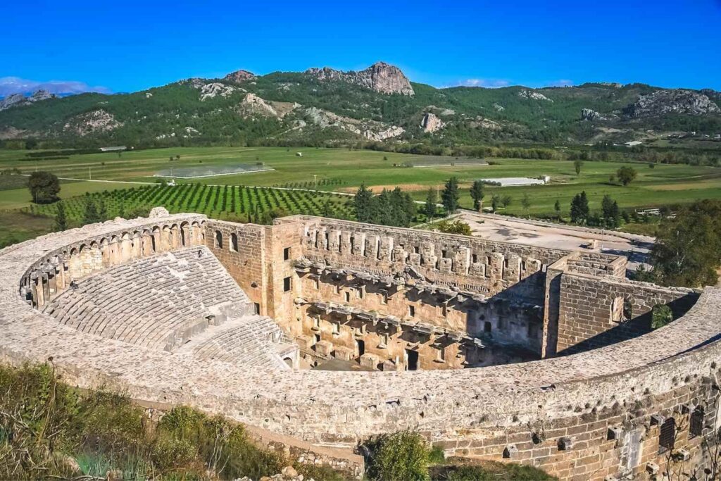 The well-preserved Aspendos Ancient Theater featuring a grand semicircular seating area and stone stage backdrop.