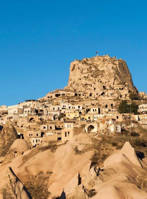 Uçhisar Castle in Cappadocia, a towering rock formation surrounded by ancient cave dwellings under a clear blue sky.