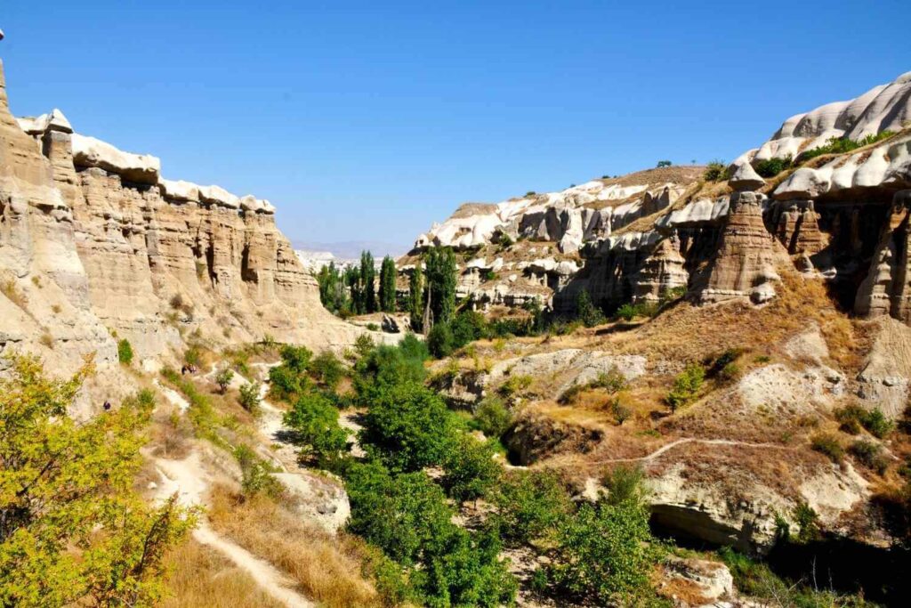 Gulludere Valley in Cappadocia with steep cliffs, greenery, and a rugged hiking path under a clear blue sky.