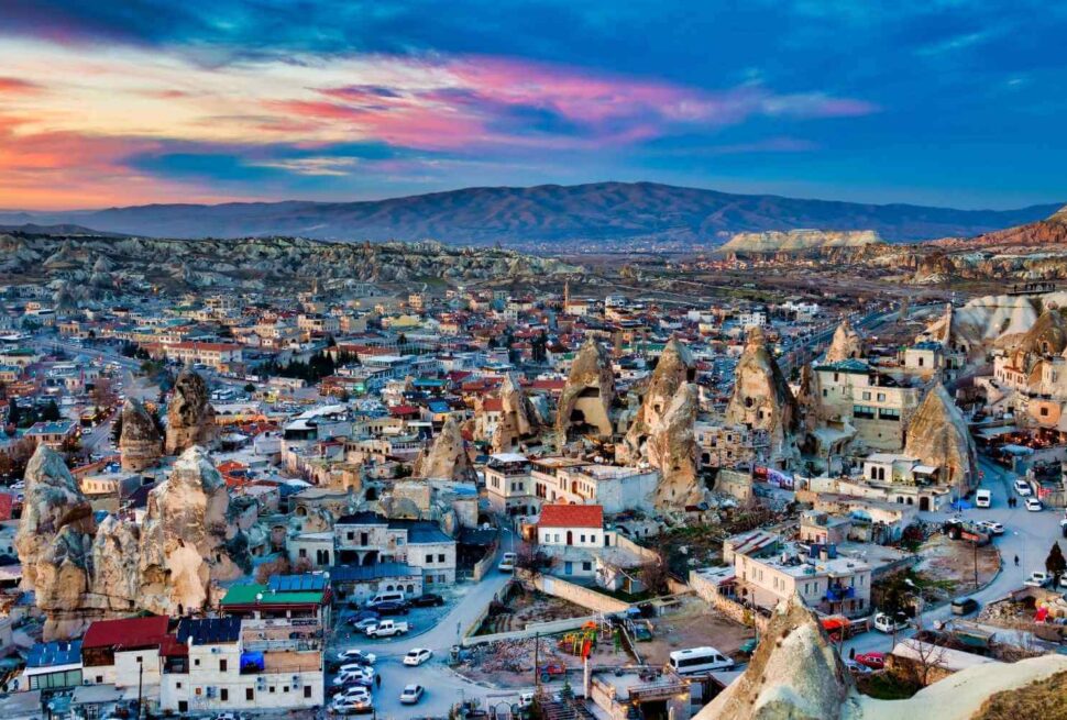 Scenic view of Cappadocia at sunset, showcasing unique rock formations, cave dwellings, and a colorful sky.