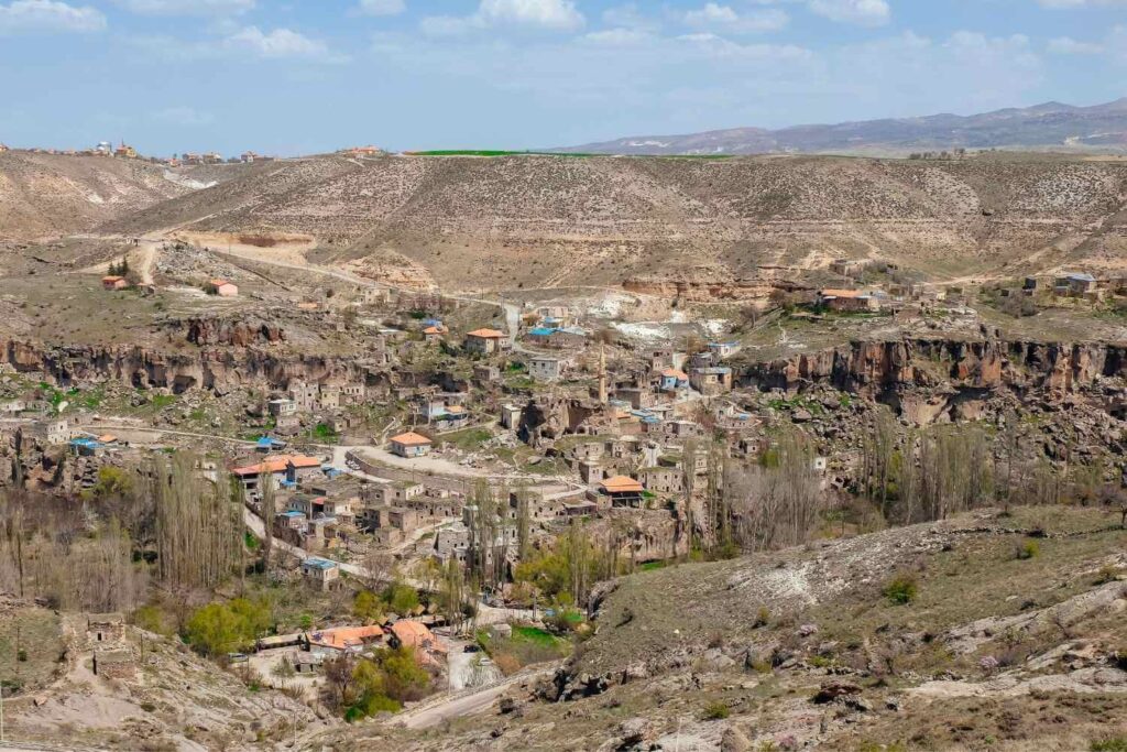 Aerial view of a historic village nestled in a rocky valley, surrounded by rugged hills under a blue sky.A scenic aerial view of an ancient village built within a rocky valley, showcasing traditional architecture amidst rugged, hilly terrain.