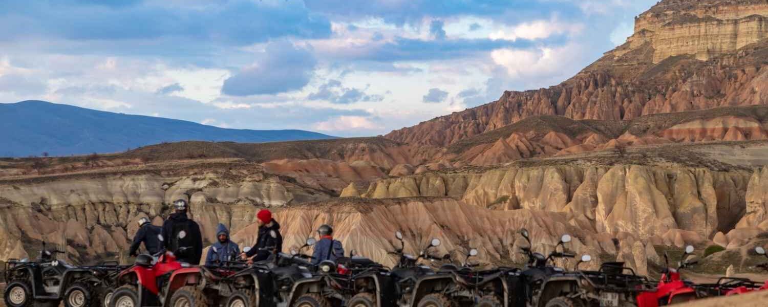 Group of ATVs lined up in Göreme's Red Valley with riders preparing for a sunset tour, surrounded by unique rock formations.