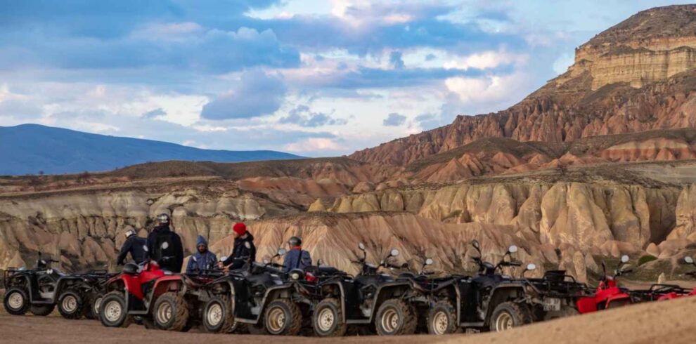 Group of ATVs lined up in Göreme's Red Valley with riders preparing for a sunset tour, surrounded by unique rock formations.