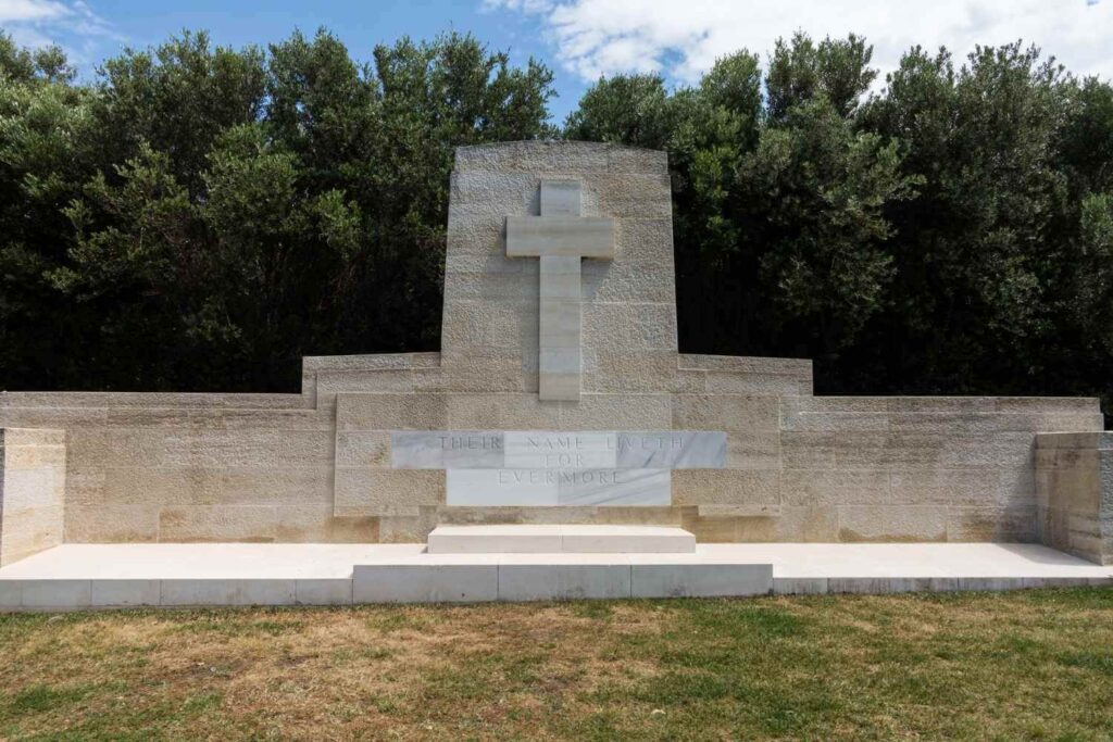 Stone memorial with a cross and engraved inscription, surrounded by greenery, honoring fallen soldiers.