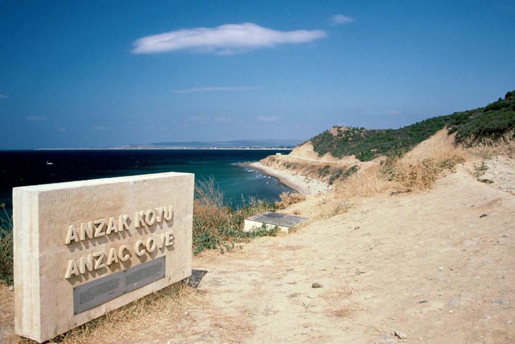 Stone monument at Anzac Cove overlooking a curved coastline, with clear blue sea and sky in the background.