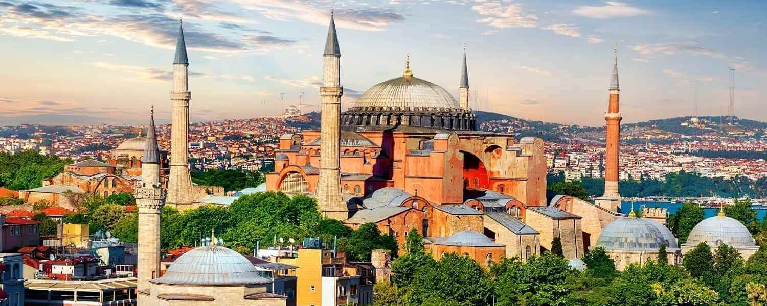 Aerial view of Hagia Sophia in Istanbul with its domes and minarets, surrounded by the cityscape under a cloudy sky.