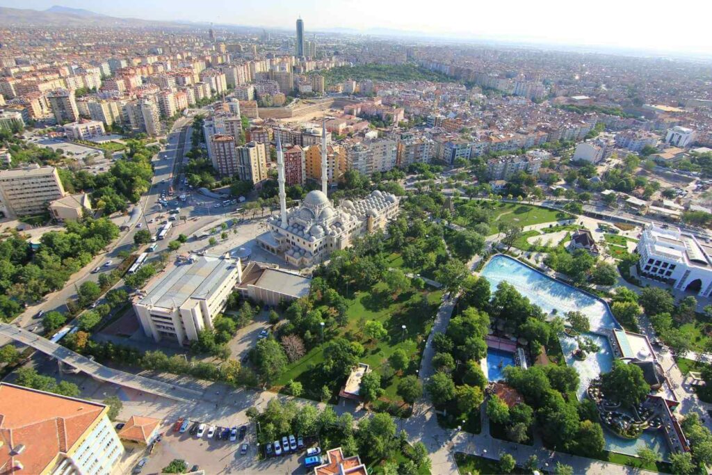 Aerial view of a cityscape featuring a large mosque with domes and minarets, surrounded by greenery, roads, and urban buildings.