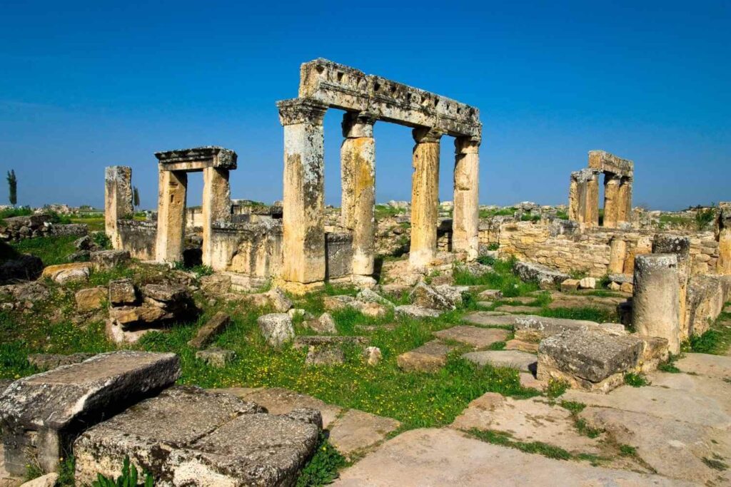 Ancient ruins of Hierapolis in Pamukkale, Turkey, showcasing weathered stone columns and arches against a clear blue sky.