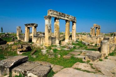 Ancient ruins of Hierapolis in Pamukkale, Turkey, showcasing weathered stone columns and arches against a clear blue sky.