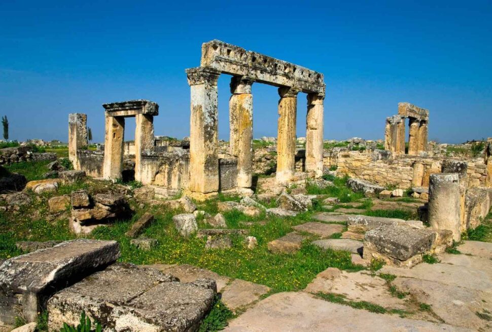 Ancient ruins of Hierapolis in Pamukkale, Turkey, showcasing weathered stone columns and arches against a clear blue sky.