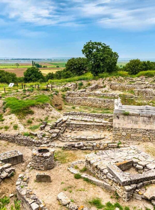 Ruins of ancient Troy featuring stone walls and foundations, set against a scenic landscape and cloudy sky.