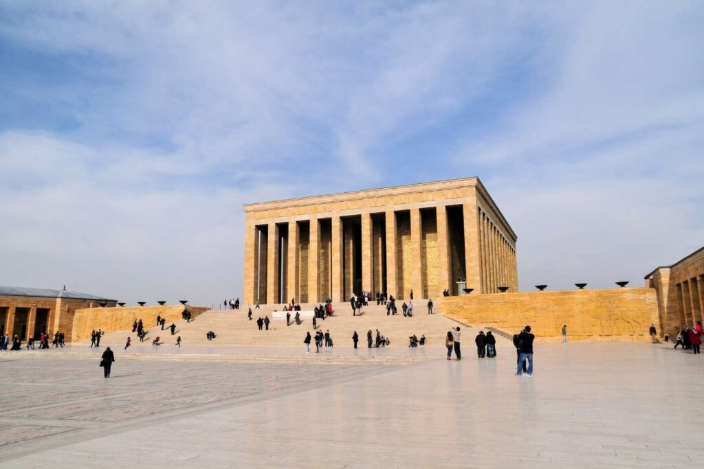 Wide-angle view of the Mausoleum of Atatürk in Ankara, Turkey, showcasing its grand columns and large courtyard with visitors exploring.