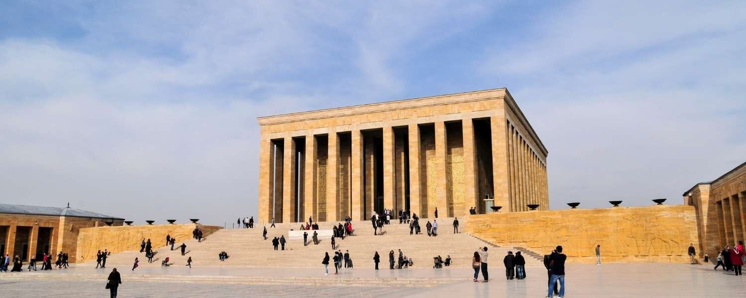 Wide-angle view of the Mausoleum of Atatürk in Ankara, Turkey, showcasing its grand columns and large courtyard with visitors exploring.