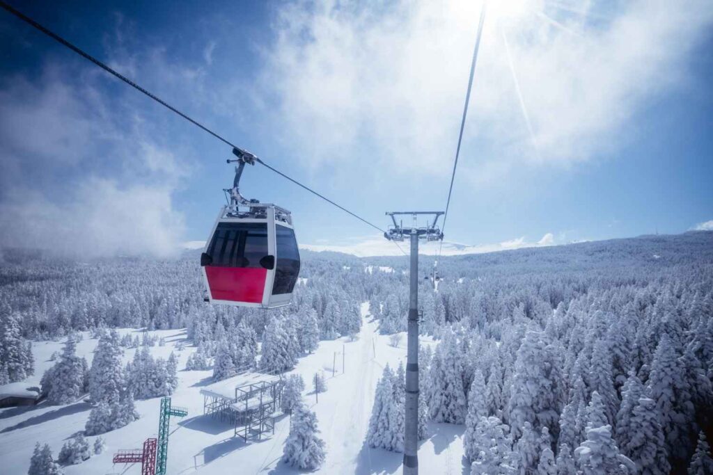 Cable car ascending over snow-covered trees in Uludağ Mountains, Bursa, Turkey, with clear blue skies and scenic winter views.