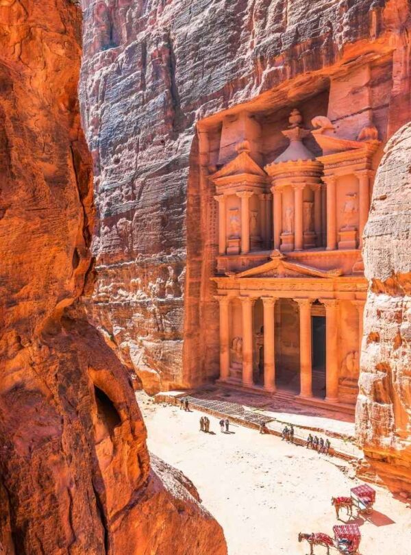 Petra Treasury carved in red sandstone cliffs with tourists and camels in the foreground, showcasing the ancient architecture of Jordan’s UNESCO World Heritage site.